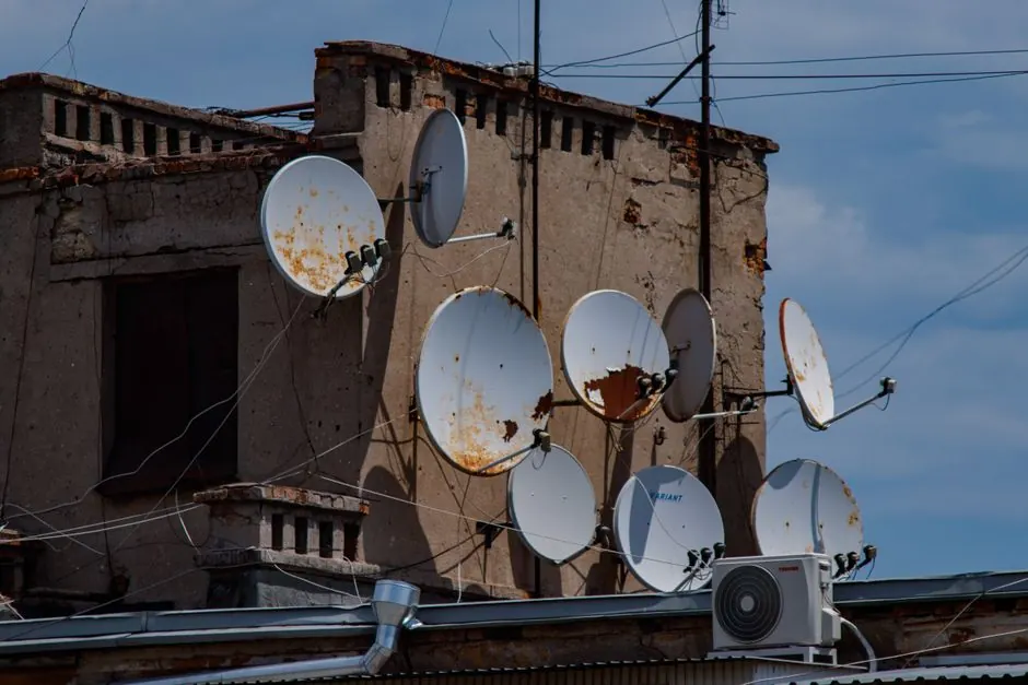 A collection of rusty satellite dishes mounted on an old urban building rooftop.
