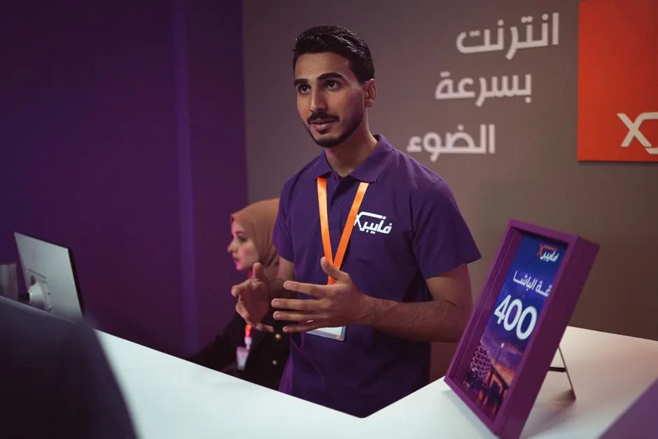 Man at a tech booth explaining features to a customer indoors with promotional banner.