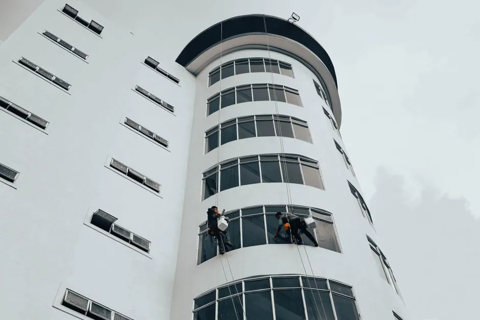 Workers cleaning windows on a modern high-rise building using ropes. Urban architectural maintenance.